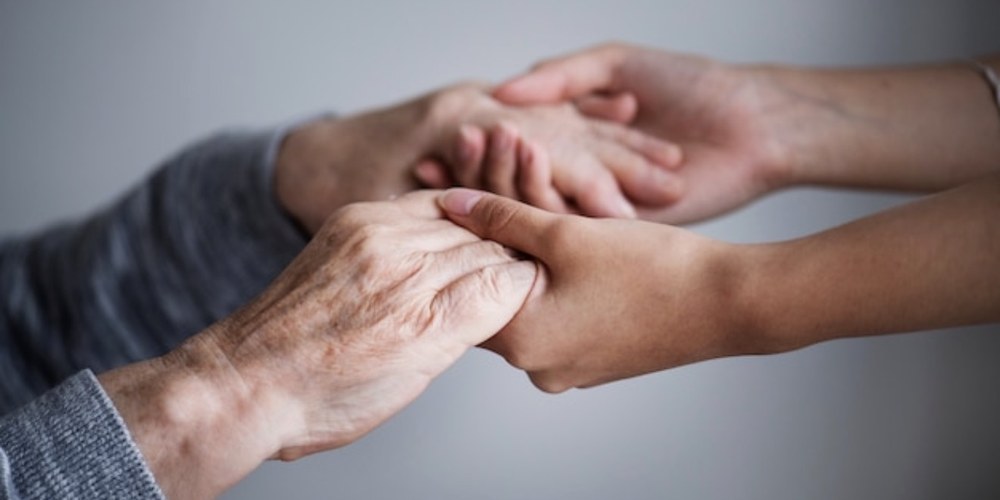 An adult child gently holding an older parent’s hand