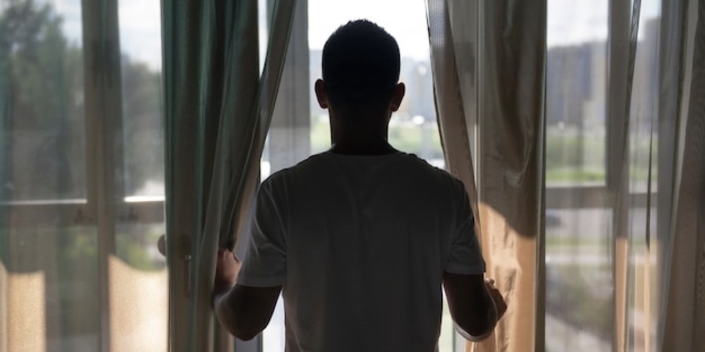 A person seated near a window looking watchful in a calm, safe home
