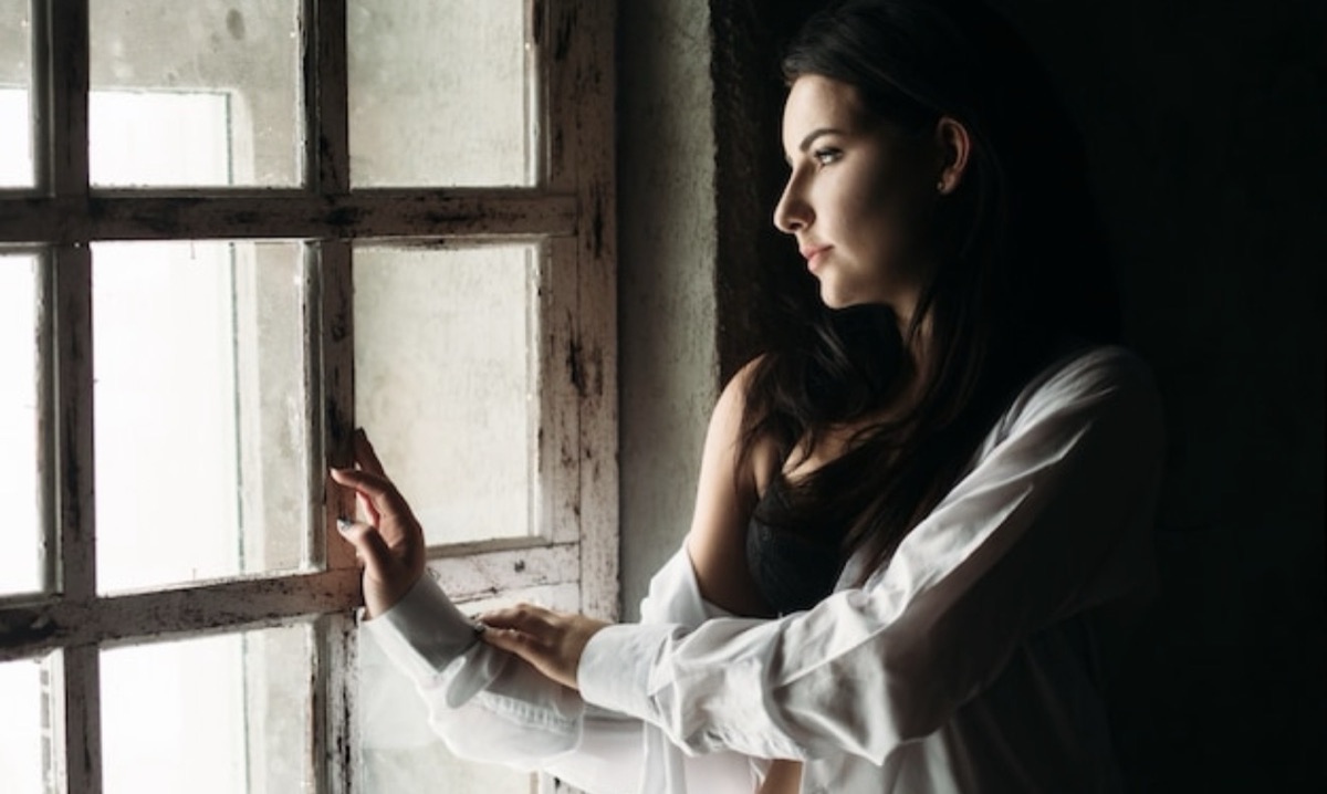 A woman standing by a window, lost in thought